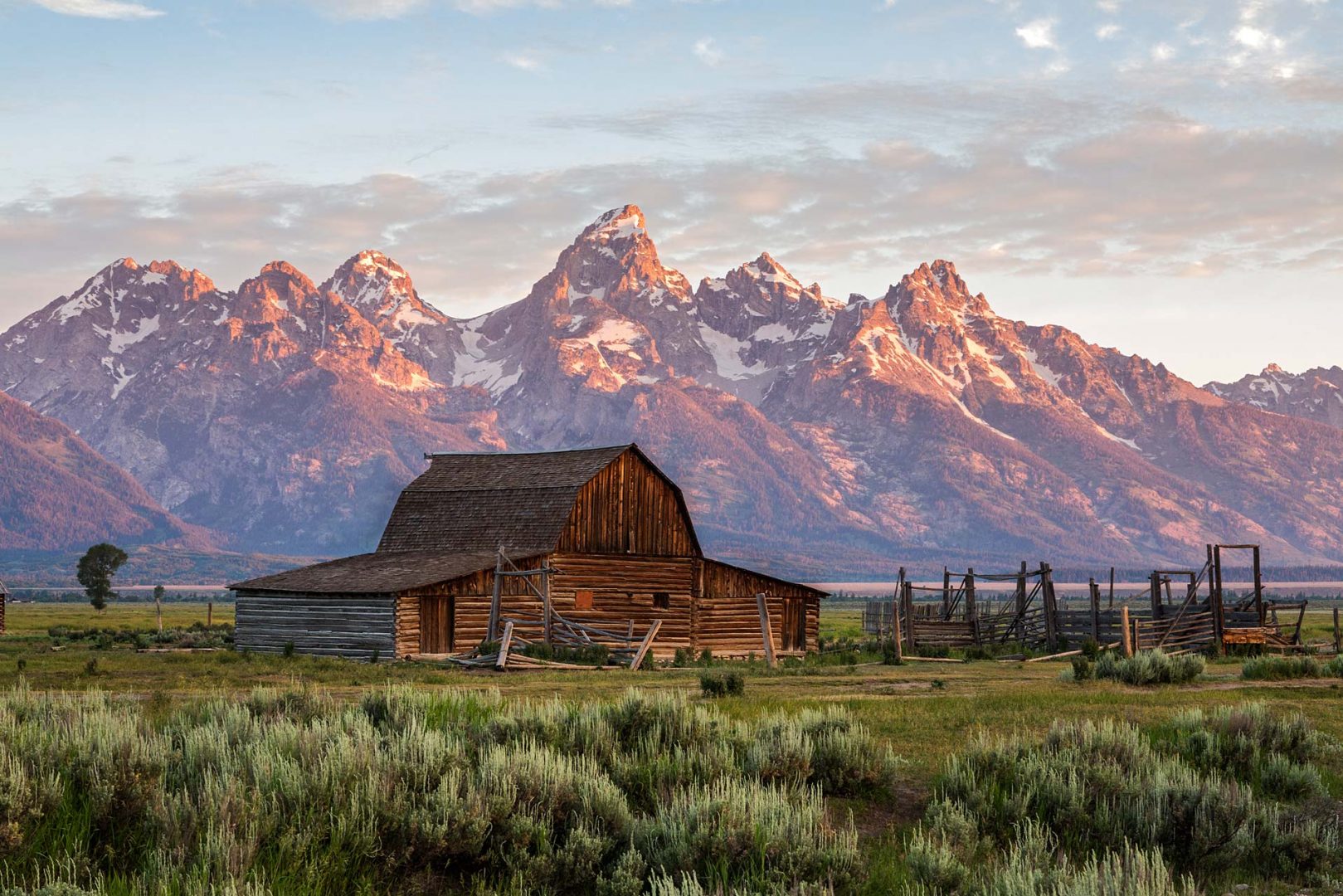 rustic barn with sun shining on the grand teton mountains in the background