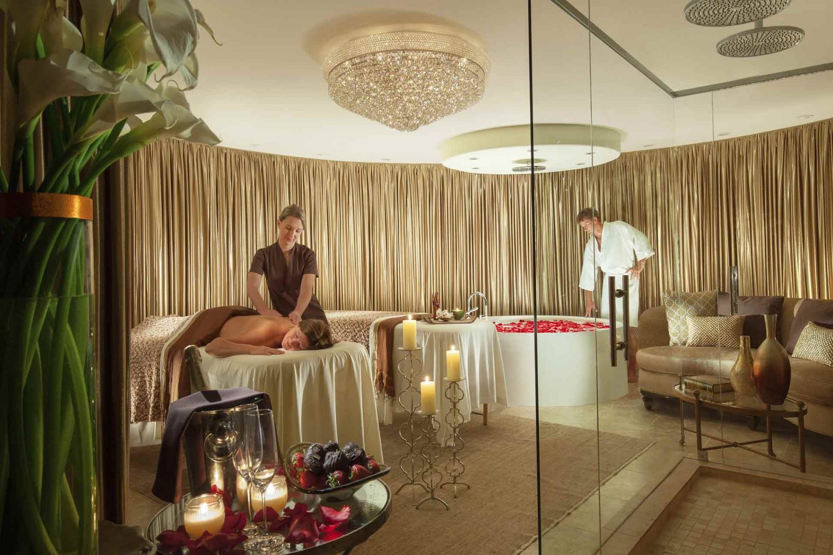 spa suite with woman getting a massage and a man looking into a jacuzzi with flowers